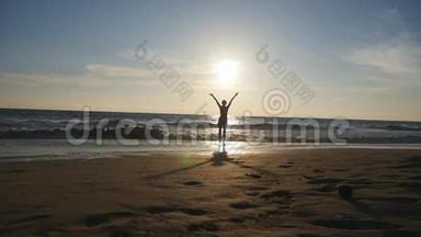 日落时分，年轻女子在海边散步，举起双手。 美丽的少女站在海边