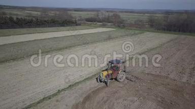 一名农民在一辆拖拉机上，带着播种机在村庄地区的一个私人田地里播种谷物。 弹簧场的机械化