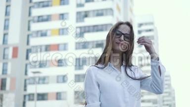 一个可爱的女孩站在城市背景上，穿着商务服。 头发随风而动。 慢节奏