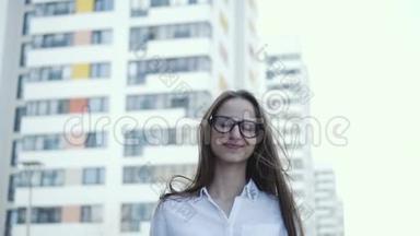 一个可爱的女孩站在城市背景上，穿着商务服。 头发随风而动。 慢节奏
