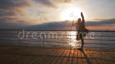 日出时，一位身穿黑色芭蕾舞裙的芭蕾舞女舞女在海堤上或海边的美丽景色