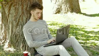 在温暖的夏日，年轻的学生坐在树<strong>下</strong>，拿着笔记本电脑工作