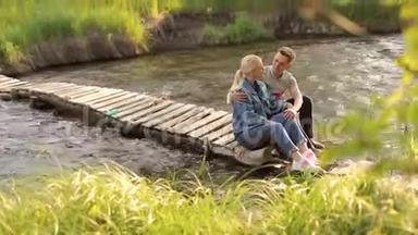 年轻夫妇<strong>坐</strong>在河边的桥上<strong>拥</strong>抱。