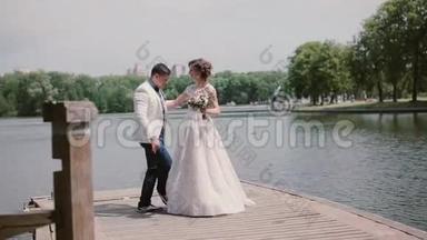 新婚之日快乐的一对，在码头上跳舞，玩得开心。夏天公园里的河流。<strong>婚礼服</strong>装