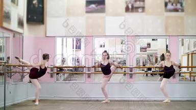在舞厅里，穿着黑色紧身衣的年轻芭蕾舞女演员优雅地站在酒吧里，站在镜子旁边