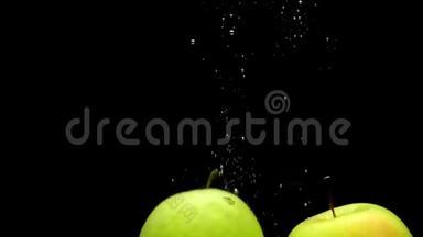 黄色和绿色的苹果在黑色的背景下落入透明的水中