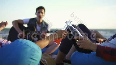 一群朋友喝着鸡尾酒和啤酒，坐在沙滩上的安乐椅上，听着一首歌