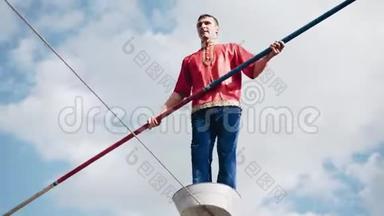 一个手里拿着杆子的人在绳子上跳.. 地面上的危险特技。