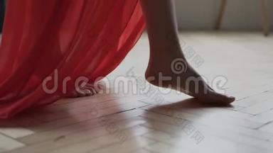 穿着红色长裙的白种人女孩的腿<strong>赤脚</strong>在房间的地板上行走。 女人<strong>走路</strong>通过相机慢镜头