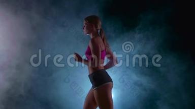 运动健身女孩在黑色背景上奔跑，被烟雾中的聚光灯照亮。 慢动作。 关门