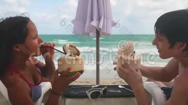 年轻漂亮的夫妇在日光浴床上放松，在苏梅岛海滨的异国度假胜地喝椰子鸡尾<strong>酒</strong>。 3840x2160，4k