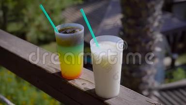 在阳光明媚的阳台上，一杯多汁的分层鸡尾酒和一杯牛奶混合饮料站在扶手里