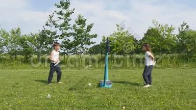 青少年男孩和女孩在草地上打羽毛球，背景是森林。 手持羽毛球拍的儿童
