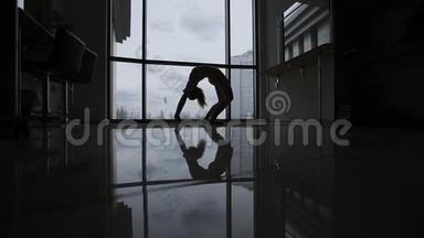 窗户旁的不可思议的体操运动。 工作室里的一个年轻的美女和镜子里迷人的倒影