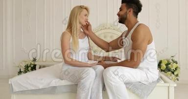 情侣相爱相拥微笑坐床面对面混血男人抚摸女人脸拥抱早间卧室