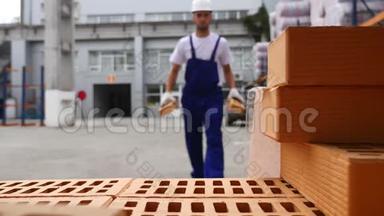 仓库工人检查红砖堆成立方体。 库存的砖块红色块。 仓库砖。 储存