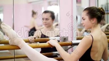 在舞厅里，穿着黑色紧身衣的年轻芭蕾舞女演员优雅地站在酒吧的镜子前站在酒吧旁边