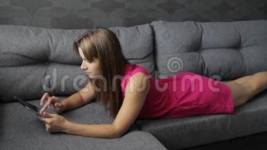 穿裙子的女人躺<strong>在</strong>沙发上的平板电脑上。 <strong>趴在</strong>肚子上.. 可爱的女人<strong>在</strong>家