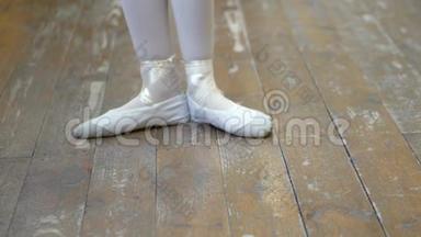 在芭蕾训练期间，一个穿白色芭蕾舞鞋的女孩`在一个旧木地板上的腿特写。 古典元素