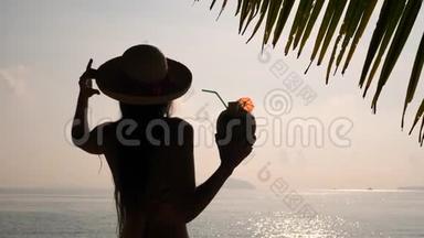 在热带海滩喝新鲜泰国椰子鸡尾酒的年轻<strong>旅游</strong>女孩日落剪影。 4K，慢动作。 <strong>普吉岛</strong>