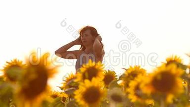 快乐的女孩，头发在风中飞扬，走在黄色的向日葵里，田野里开着金色的花，夏天阳光明媚的一天。