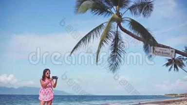 棕树<strong>下</strong>的沙滩上，一位身穿红色连衣裙、戴着墨镜、带着手机拍照的美女