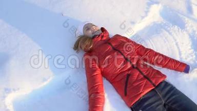美丽的年轻女子在冬天的公园里做雪天使，玩得很开心，微笑着。 慢动作。