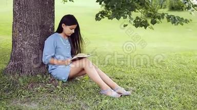 一个留着长发的漂亮小女孩在阳光明媚的日子里，坐在树<strong>下</strong>看书