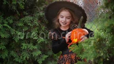 万圣节的小女巫在秋天的树叶背景下，女孩拿着南瓜点燃蜡烛亲吻