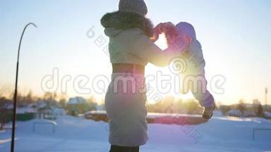 女孩在冬天日落时和婴儿玩。 双手环抱