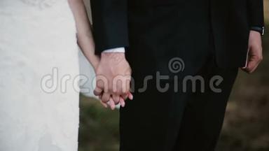 婚礼上新郎新娘牵手的特写镜头。 穿着婚纱的女人靠近男人拿着花束。