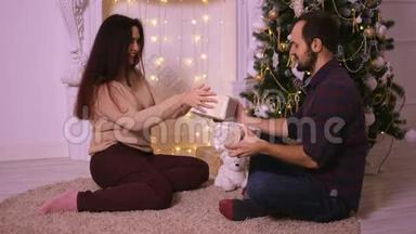 幸福的年轻夫妇坐在壁炉旁互相送礼物。 圣诞快乐。