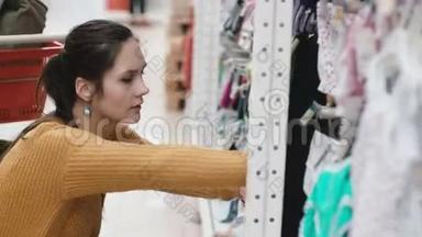 年轻漂亮的女人蹲在超市，在<strong>橱窗</strong>里挑选婴儿<strong>服装</strong>。 女的在店里。 4K