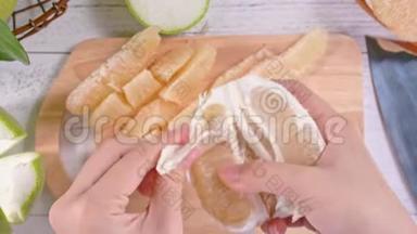 年轻的亚洲妇女正在剥鲜蜜柚，在明亮的白色木桌和砧板上的家庭厨房里吃，顶部的景色。