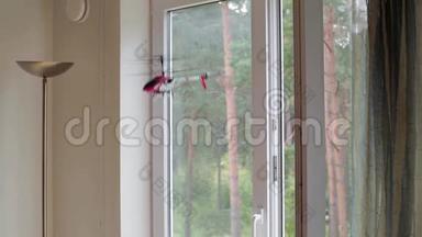 红纳米直升机在白天的房间里飞行，白色的墙壁和大窗户