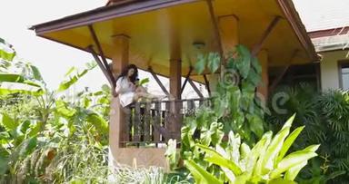在热带森林的别墅里，年轻女子坐在阳台上使用手机，漂亮女孩在户外<strong>上网聊天</strong>