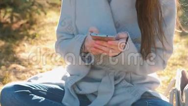 年轻漂亮的黑发女人坐在<strong>春天</strong>公园的草地上，用<strong>手机</strong>输入一条信息。 特写双手。