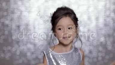 美丽的微笑的小女孩，穿着银色的裙子，在银色的背景下跳舞。