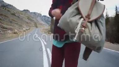 旅行者女人拿起她的背包。 在清晨的乡村里，背包客女人把包从马路上<strong>提起</strong>来