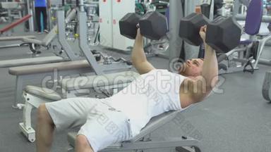 健美运动员在健身房用哑铃做长凳按压。 肌肉男在健身房锻炼