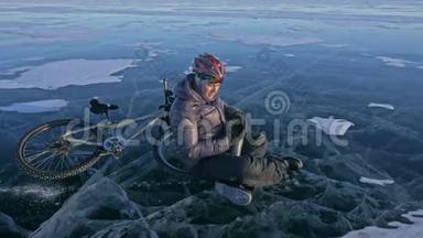 那个人正坐在冰上自行车的轮子上休息。 他喝热水瓶里的茶。 骑自行车的人穿着