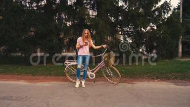 姜红头女孩坐在自行车上，在夏<strong>季</strong>公园的智能手机上发短信。 穿着<strong>粉色</strong>衬衫和牛仔裤