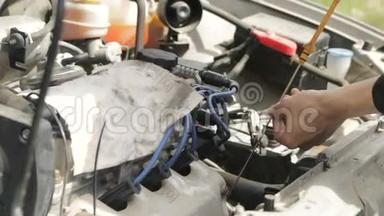 在汽车的引擎盖下面，一个男人用油尺在汽车车间检查机油油位