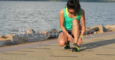 健康的生活方式健身女跑步者在阳光明媚的海边跑步前系鞋带