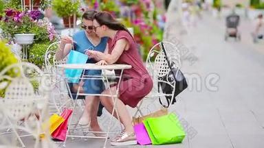 两位<strong>时尚</strong>的五颜六色的<strong>购物</strong>者带着袋子在露天咖啡馆<strong>购物</strong>。 售，消费主义和人的观念.. 高加索女孩