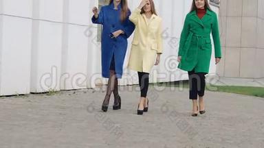 三个放心的女人穿着羊绒羊毛外套走在街上。 慢慢地