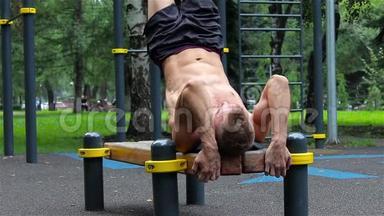 运动员在夏季树木下在城市公园的长凳上锻炼腹肌，以进行<strong>运动健身</strong>。 腹肌 特写