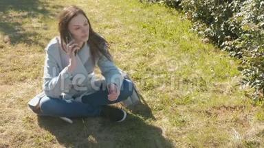 年轻漂亮的女人坐在草地上的春天公园里，用手机说话。