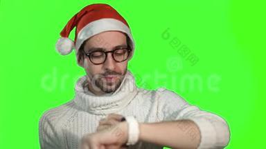 戴着圣诞老人帽子、戴着智能手表在绿色背景下触摸屏幕的粗鲁严肃的人