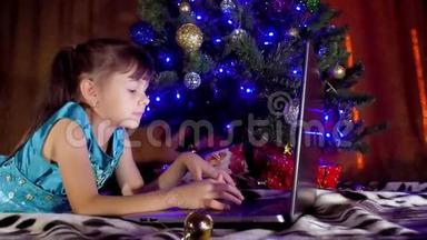 圣诞树下有笔记本电脑的女孩。 在新年里，孩子在一棵树下，手提电脑。 一个小女孩